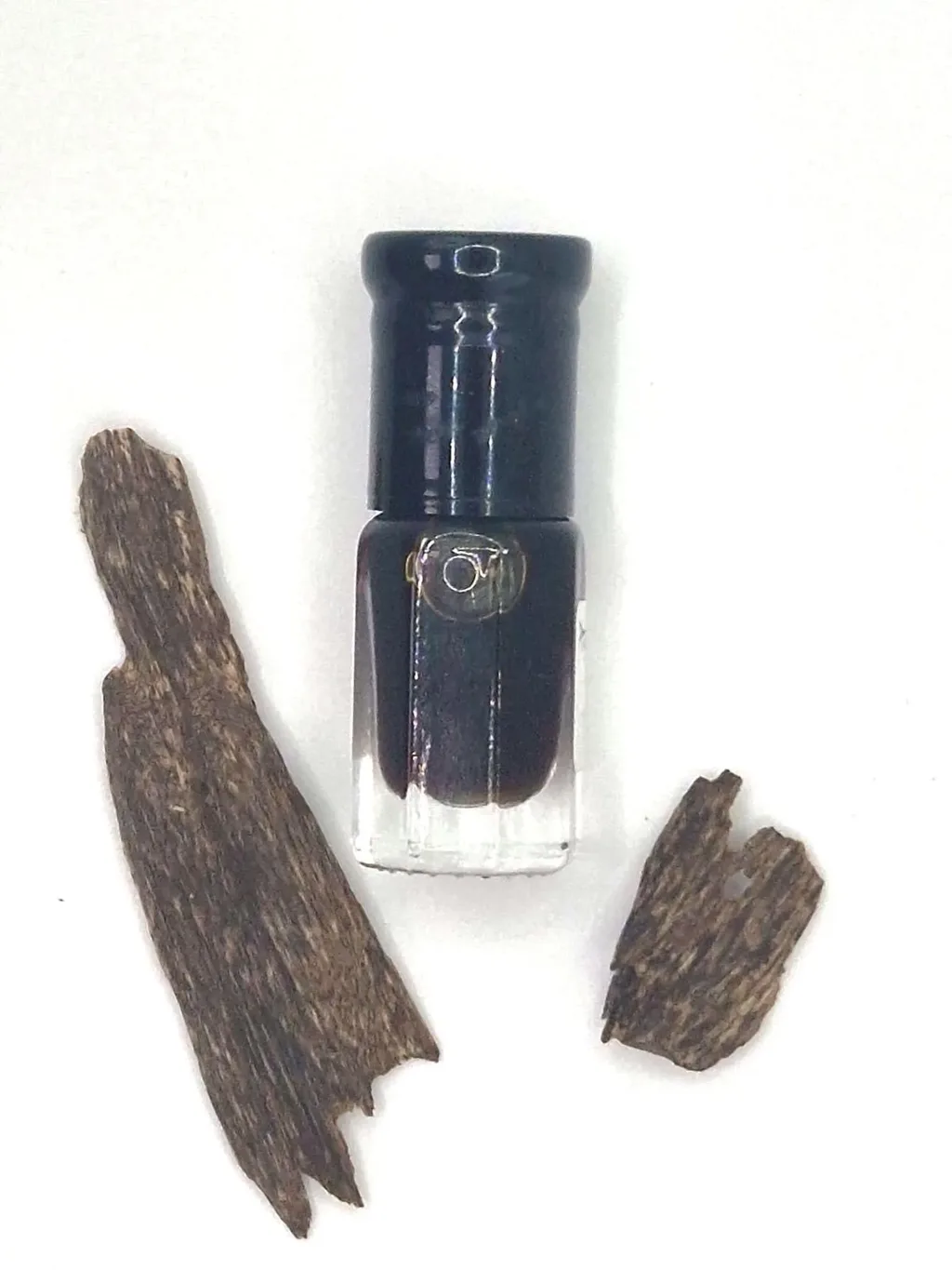Original supplier photo of a small perfume bottle shot flat on a white background next to two pieces of agarwood, with uneven lighting.